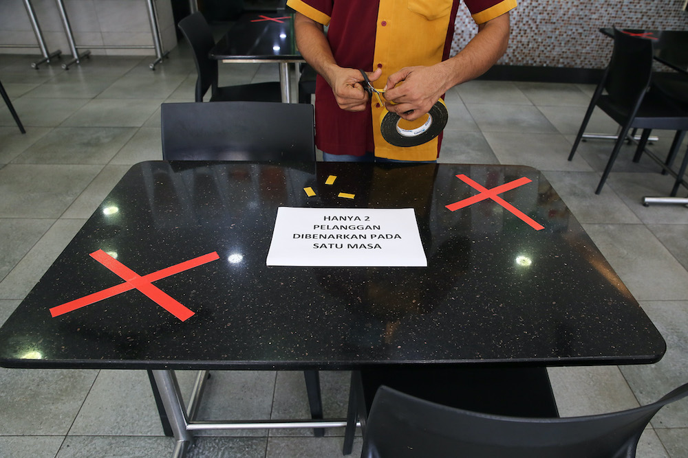 A worker places a notice stating that only two customers are allowed per table at Khulafa Restaurant in Shah Alam May 2, 2020. u00e2u20acu201d Picture by Yusof Mat Isa