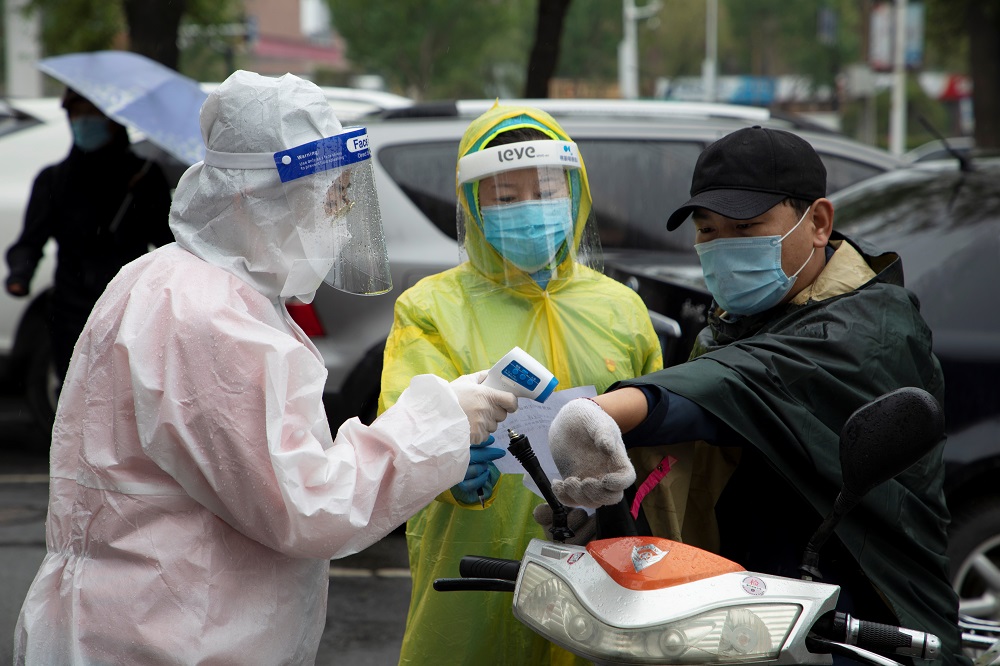Volunteers in protective gear measure the body temperature of a man at the entrance of a residential compound following the Covid-19 outbreak, in Chuanying district of Jilin, China May 22, 2020. u00e2u20acu201d Picture by China Daily via Reuters