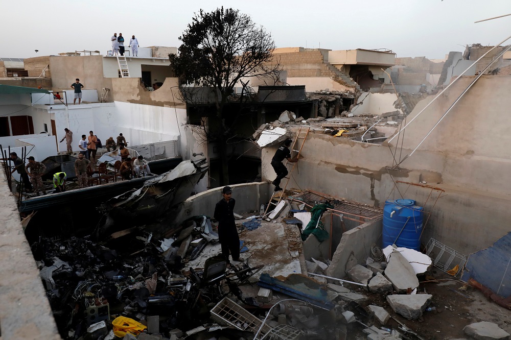 People stand on a roof of a house amidst debris of a passenger plane, crashed in a residential area near an airport in Karachi May 22, 2020. — Reuters pic
