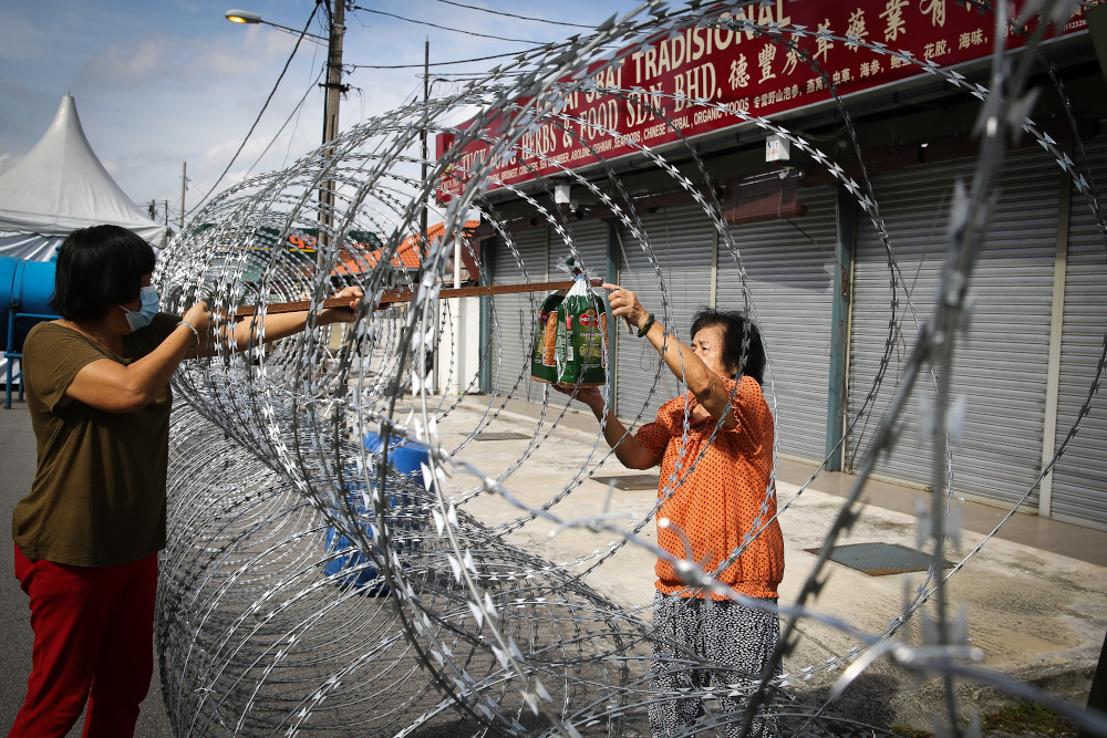 Retiree Wong Ai Kwok (right) collects supplies through barbed wire fencing in PJ Old Town, Petaling Jaya May 12, 2020. — Picture by Yusof Mat Isa