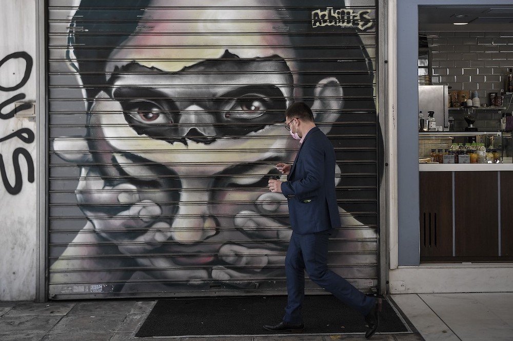 A man wearing a protective facemask walks past a graffiti by Greek street artist Achilles in central Athens on May 8, 2020. u00e2u20acu201d AFP picnn