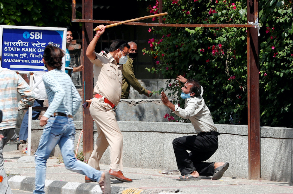 A police officer raises a baton at a man who, according to police, had broken the social distancing rule, outside a wine shop during an extended nationwide lockdown to slow the spread of the coronavirus disease, in New Delhi, India, May 4, 2020. u00e2u20acu201d Reute