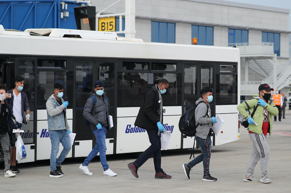 Refugees and migrants from overcrowded migrant camps who will be transferred to Britain wear protective face masks as a precaution against the coronavirus disease as they walk to 