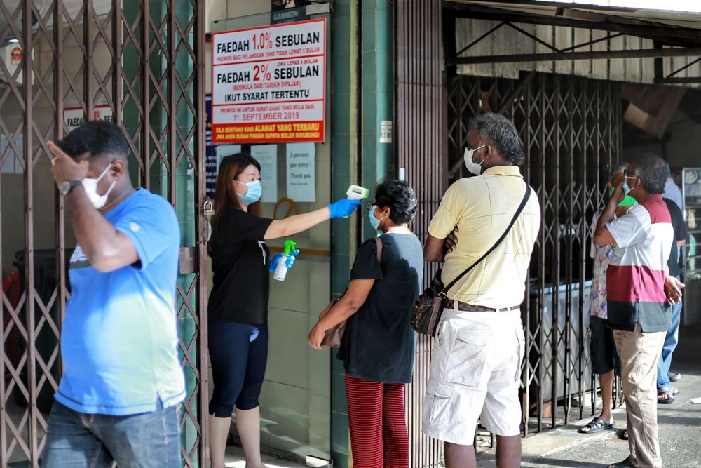 A Shin Ngien pawnshop staff conducts temperature checks on customers in SS9, Petaling Jaya May 5, 2020. — Picture by Ahmad Zamzahuri