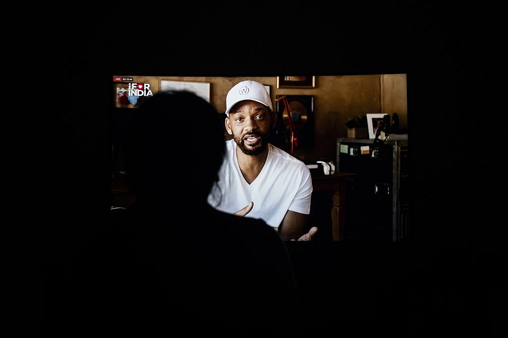 A woman watches US actor Will Smith speaking during the 'I For India' concert live on Facebook on a television screen in New Delhi May 3, 2020. u00e2u20acu201d AFP pic
