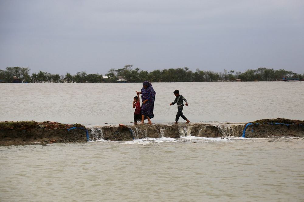 A woman with her children makes her way through a dam damaged by cyclone Amphan in Koyra, Satkhira, on May 27, 2020. At least 112 people were killed in eastern India and Bangladesh after Cyclone Amphan struck. u00e2u20acu201d AFP pic