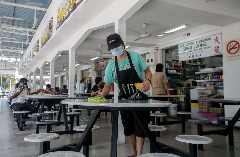 A worker is pictured wiping a table at Medan Selera Stadium Ipoh after the Perak state government lifted dine-in restrictions May 21, 2020. u00e2u20acu201d Picture by Farhan Najibnnn