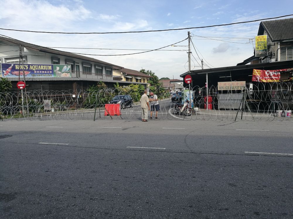 A resident collects cartons of eggs through barbed wire fencing on Jalan Pasar 1/21 in Petaling Jaya Old Town May 12, 2020. — Picture by Soo Wern Jun
