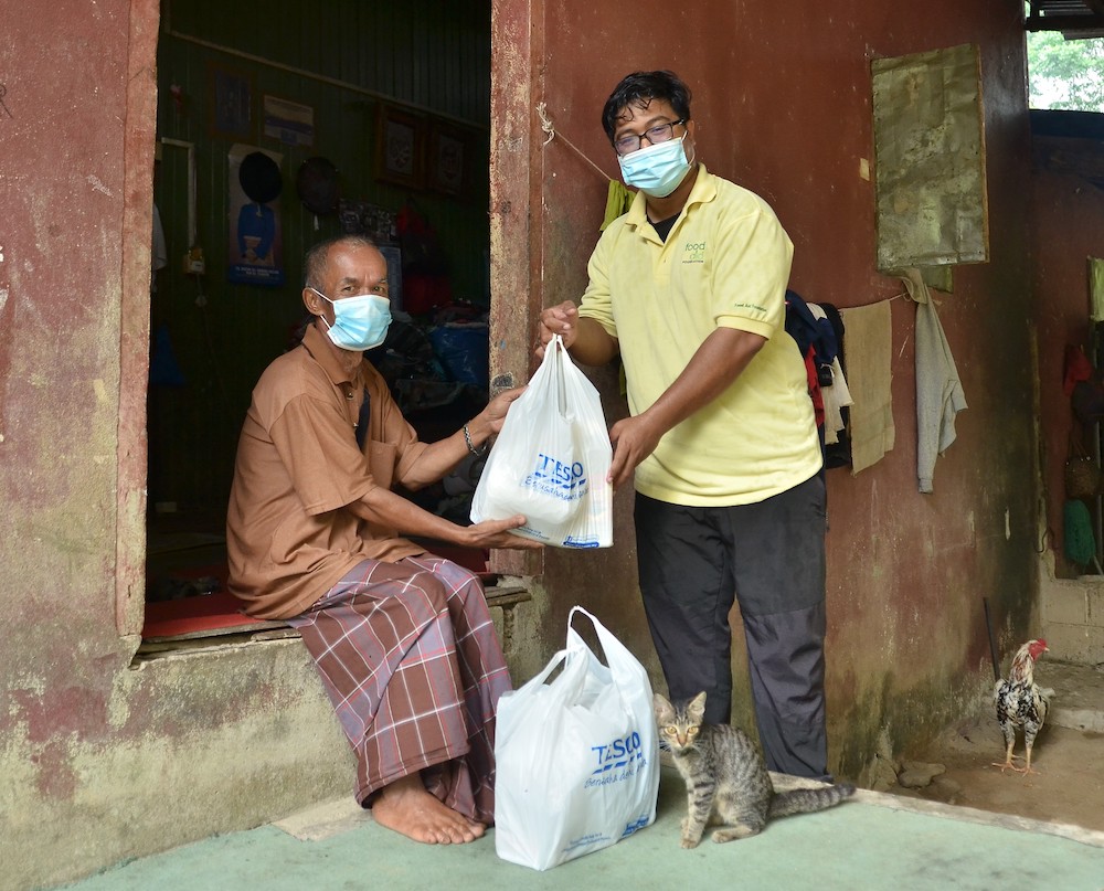 A Food Aid beneficiary (and his pet) delighted to receive the food parcel. — Picture courtesy of Tesco Malaysia