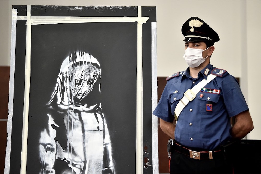 In this file photo taken on June 11, 2020, an Italian Carabinieri poses near a piece of art attributed to Banksy, that was stolen at the Bataclan in Paris in 2019, and found in Italy, during a press conference in Lu00e2u20acu2122Aquila. u00e2u20acu201d AFP pic