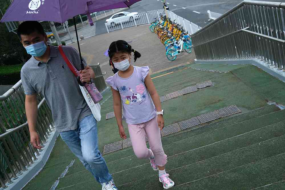 A man holds an umbrella for a girl, both wearing face masks, as they walk on an overpass amid rainfall, following the Covid-19 outbreak in Beijing, China June 29, 2020. u00e2u20acu201d Reuters pic