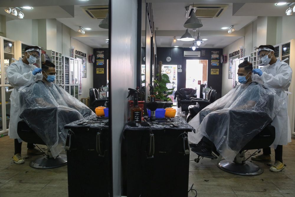 A barber wearing protective gear gives his customer a haircut at the Maginoo Barbershop in Shah Alam June 11, 2020.  u00e2u20acu201d Picture by Yusof Mat Isa