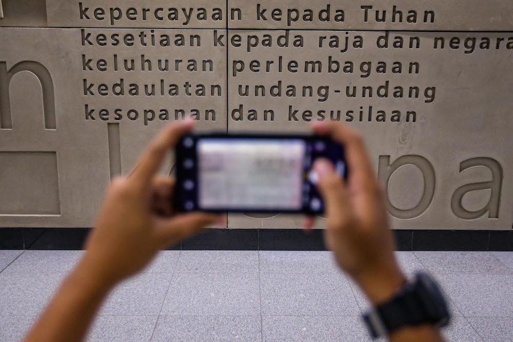 A commuter takes a photo of the Rukun Negara featured on a wall at the Merdeka MRT station. u00e2u20acu201d Picture by Hari Anggara