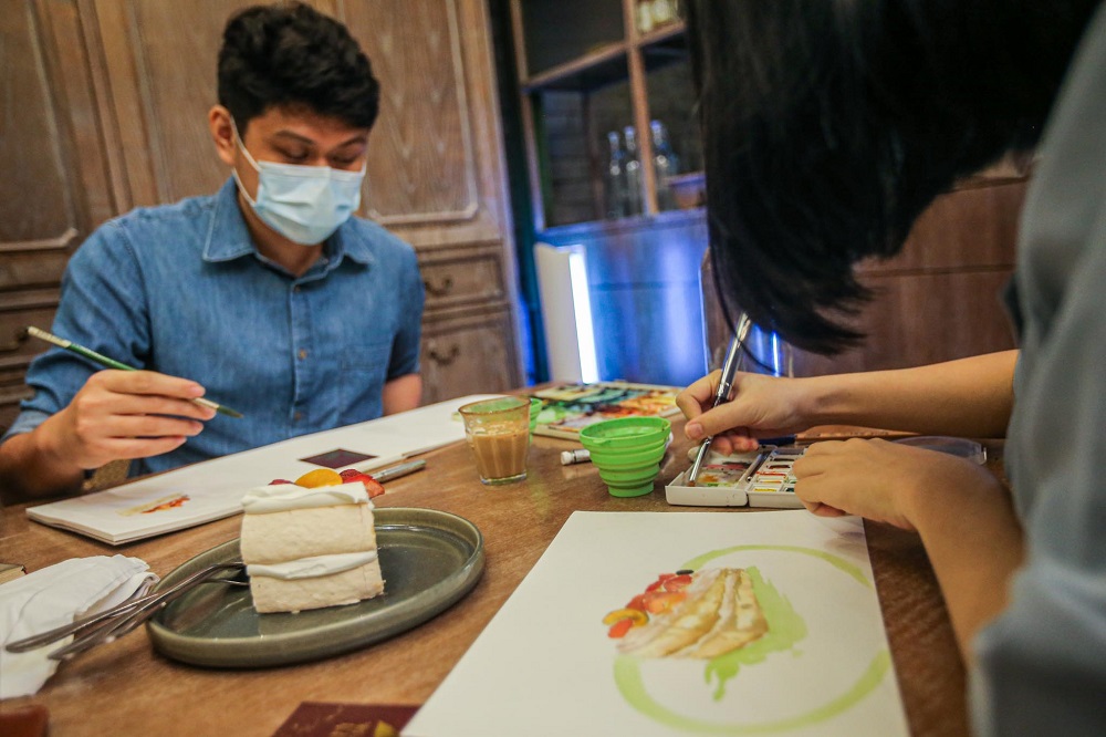 Low Tze Yang and Yong Hui Xin drawing a slice of cake placed in front of them.