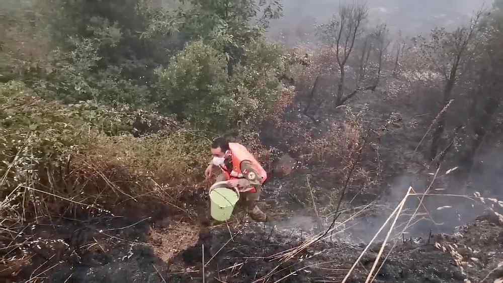 A volunteer firefighter walks to refill his bucket to control a wildfire at Monte Fundeiro, Oleiros, Portugal July 26, 2020. u00e2u20acu201d Aprosoc video image via Reuters