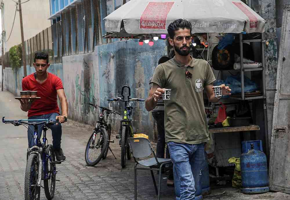Shaaban Hamuda (right), 31, a Palestinian business management graduate, serves coffee to customers, as one of his delivery employees carries a tray of steaming cups of coffee, in the southern Gaza Strip July 13, 2020. u00e2u20acu201d AFP pic