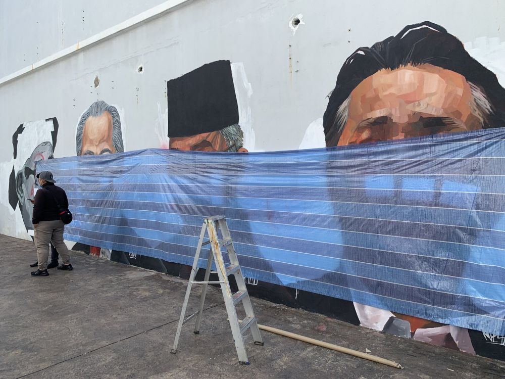 The popular mural, which is believed to have been defaced by vandals, is seen covered with a piece of tarpaulin. u00e2u20acu201d Picture via Twitter