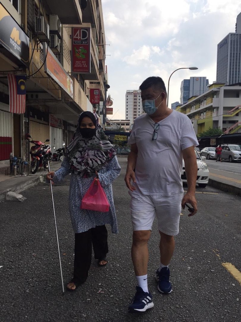 Uncle Kentang assisting a blind lady during one of his distribution runs. — Picture courtesy of Facebook/ Kuan Chee Heng 
