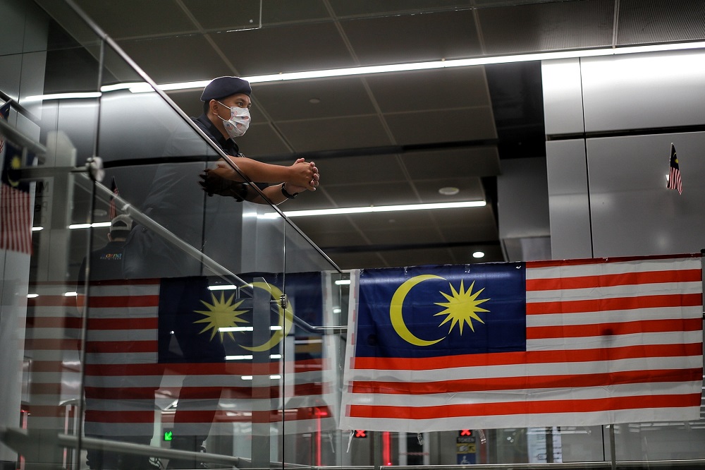 The Malaysian flag is reflected on a glass panel next to an on-duty auxiliary policeman at the Merdeka Station in Kuala Lumpur August 31, 2020. u00e2u20acu201d Picture by Ahmad Zamzahuri