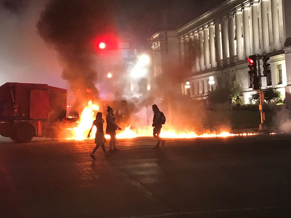 People stand near a burning vehicle in front of the Kenosha County courthouse in Kenosha, Wisconsin, in this August 24, 2020 picture obtained from social media. u00e2u20acu2022 Handout via Reuters