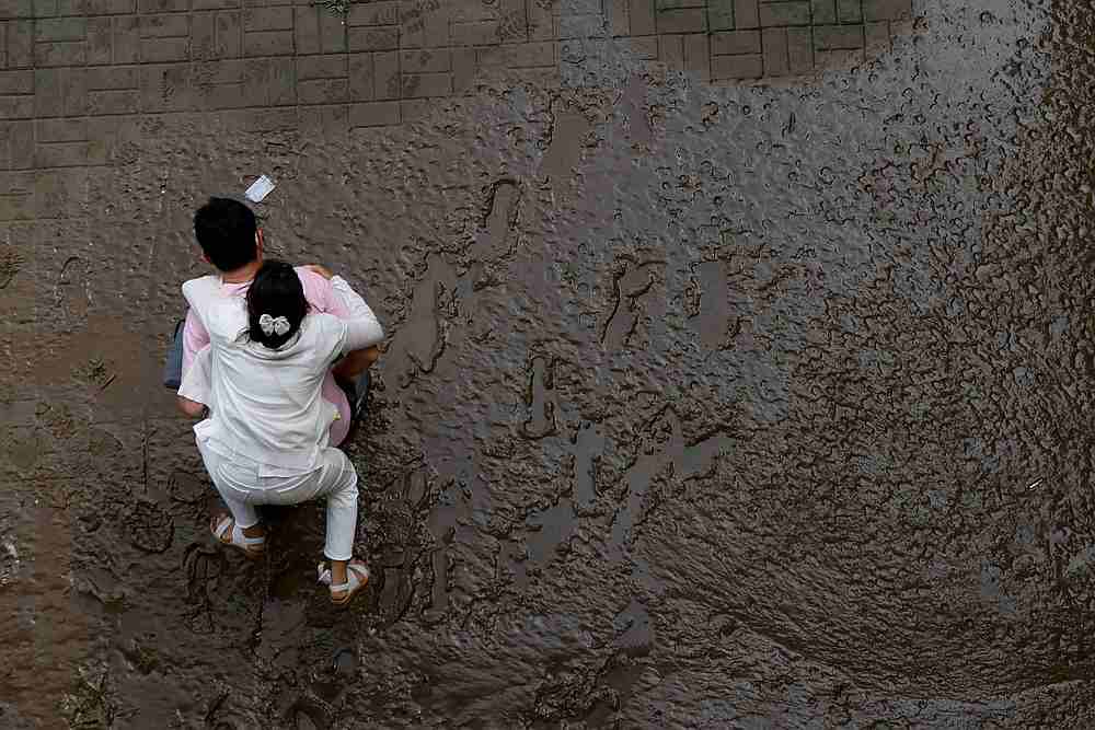 A man crosses a mud-covered trail carrying his wife on his back at a flooded Han River park in Seoul, South Korea August 4, 2020. u00e2u20acu201d Reuters pic