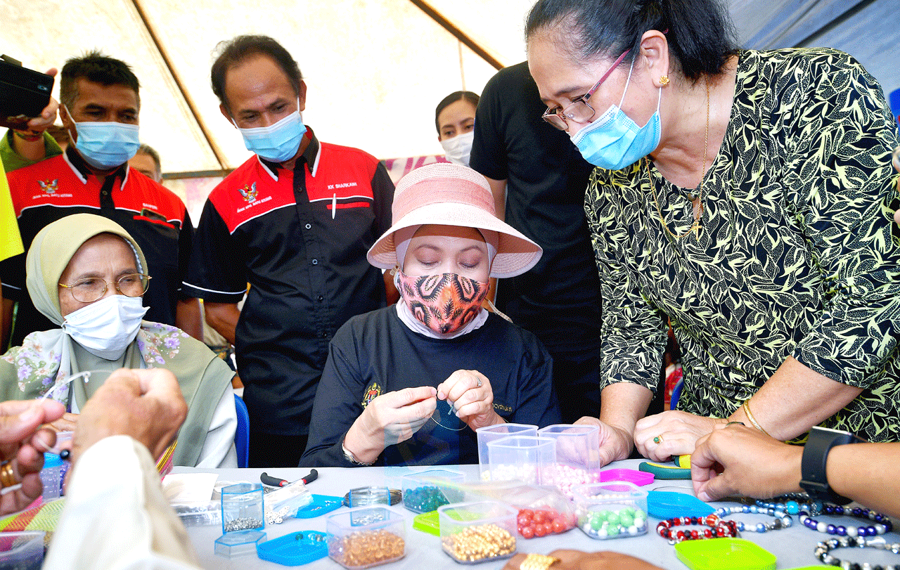 Nancy (seated, second left) tries her hands at making bead jewellery at one of the exhibition stalls set up in connection with the u00e2u20acu02dcLan Berambehu00e2u20acu2122 event in Kampung Batu Kitang Lama near Kuching. u00e2u20acu201d Bernama pic