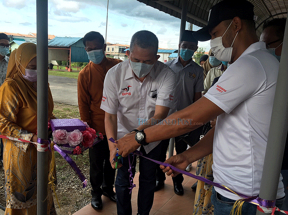 Fadillah cuts the ribbon to mark the symbolic handing-over of the schoolu00e2u20acu2122s new roofed corridor, witnessed by Fazzrudin (right) and others. u00e2u20acu201d Borneo Post Online pic