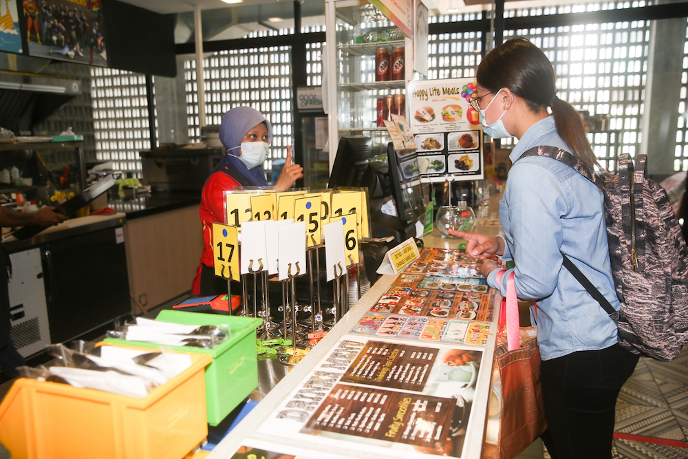 Cashier Nik Nurhidayah Ahmad Shahimi attends to a customer at the counter, where cue cards are available for diners to communicate with deaf employees. — Picture by Choo Choy May