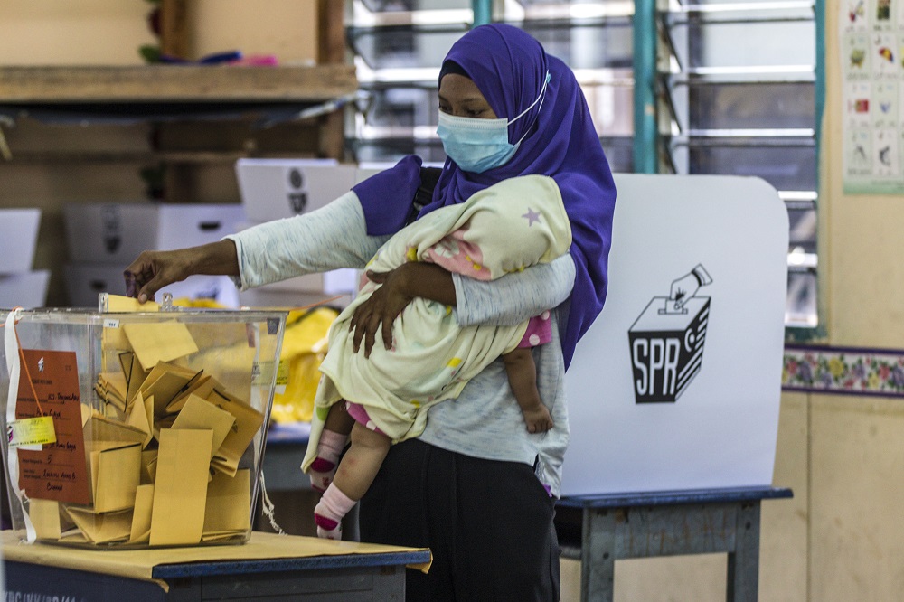 A voter cradles her child as he casts her vote at SK Pulau Gaya September 26, 2020.