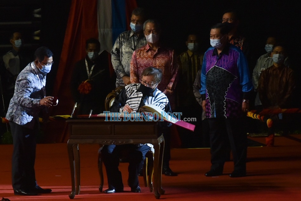 Johari signs the special Malaysia Day Book while Muhyiddin and Sabah Law and Native Affairs Minister Datuk Aidi Moktar (right) look on. u00e2u20acu201d Picture from Penerangan via Borneo Postn