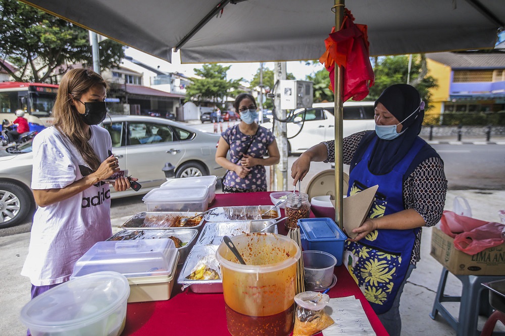 Nur Atikah Abdullah (right) serves customers at her nasi lemak stall along Jalan Telawi, Bangsar October 27, 2020. — Picture by Hari Anggara.