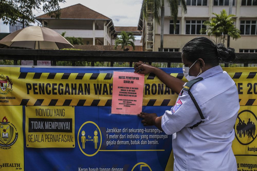 A security guard attaches a notice of closure to the gate of Sekolah Menengah Kebangsaan Bandar Utama Damansara 4 in Petaling Jaya October 12, 2020. u00e2u20acu201d Picture by Hari Anggara