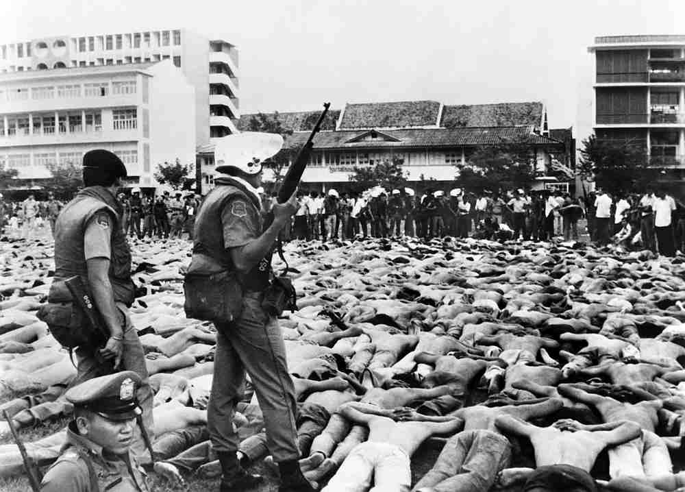 Shirtless students lie facedown on the ground, as police stand guard on the Thammasat University campus in Bangkok on October 6, 1976 when protesting students were shot, beaten to death and lynched by state forces and royalist mobs. u00e2u20acu201d AFP pic
