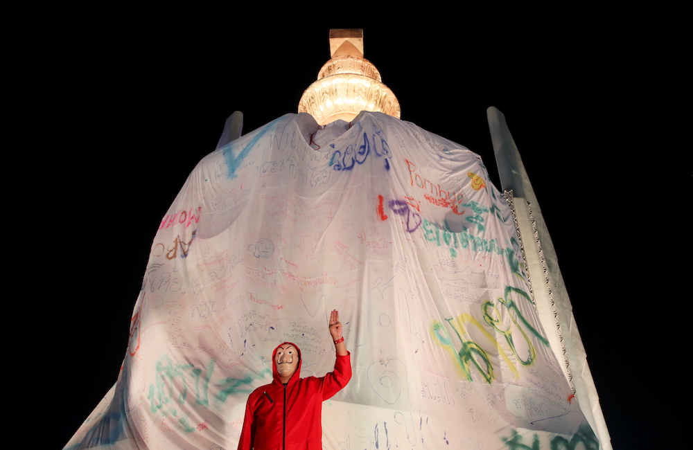 A protester shows the three finger salute in front of the Democracy Monument wrapped in a banner during a rally to call for the ouster of Prime Minister Prayuth Chan-ochau00e2u20acu2122s government and reforms in the monarchy in Bangkok, Thailand, November 14, 2020. 