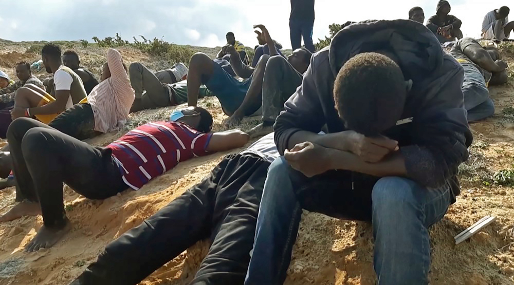 A video grab from AFPTV shows migrant survivors of a deadly shipwreck siting on a sandy beach on the coast of al-Khoms, a port city 120km west of the Libyan capital Tripoli, November 12, 2020. — AFP pic