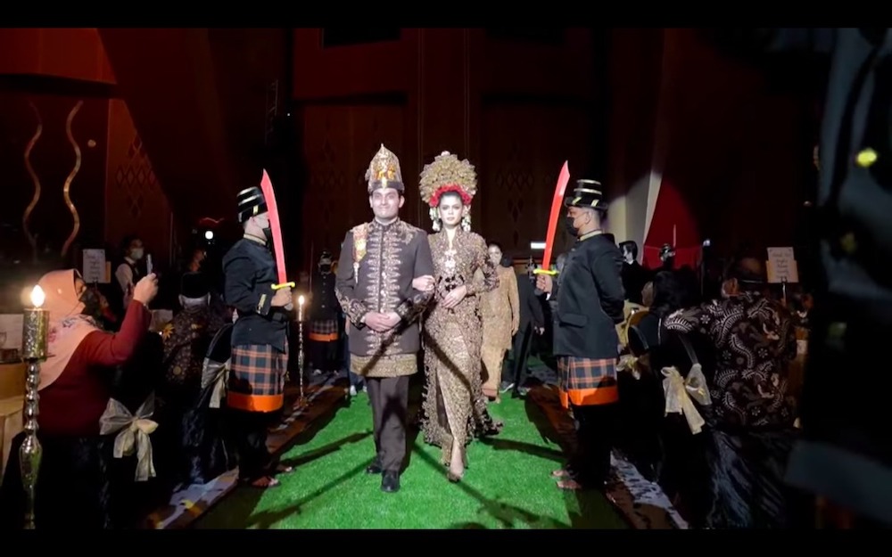 Newly-weds Tengku Muhammed Hafiz Adnan and Oceane Cyril Alagia enter the banquet hall as masked men in traditional Javanese garb stand guard.