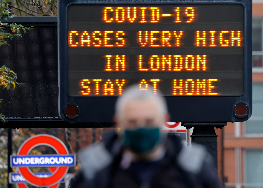 Pedestrians, some wearing a face mask or covering due to the Covid-19 pandemic, walk past a sign alerting people to stay at him in central London on December 23, 2020. u00e2u20acu201d AFP picnn