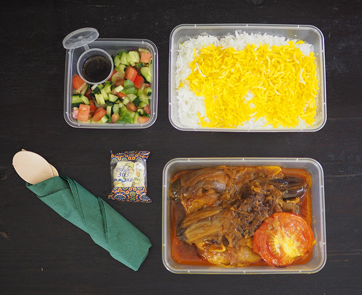 The lunchbox is made up of different containers of food and wooden cutlery with a napkin.