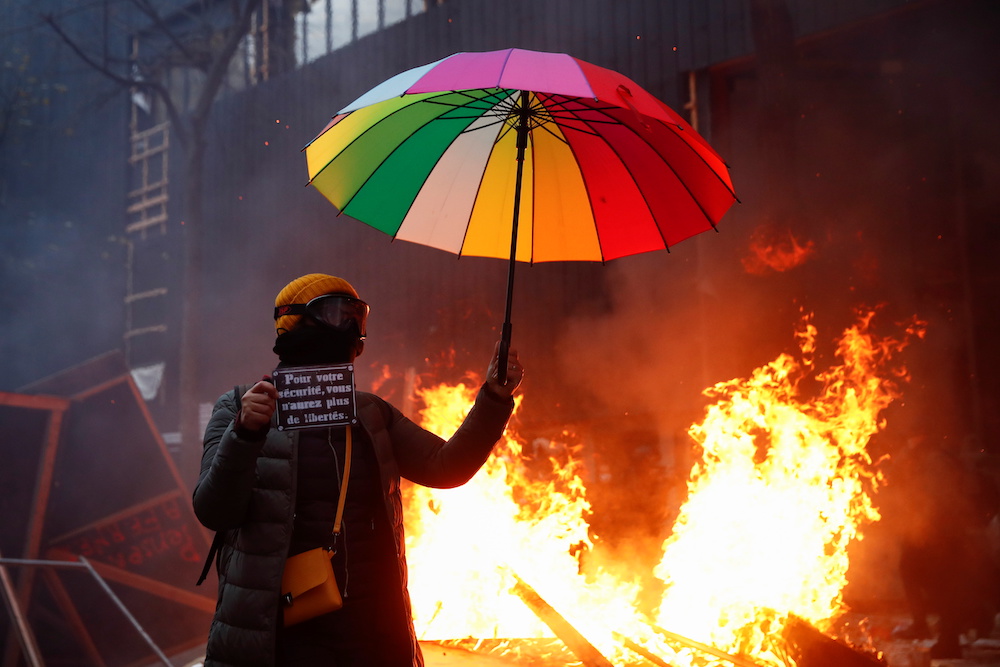 A demonstrator holds an umbrella and a sign reading u00e2u20acu02dcFor your safety you will have no more freedomsu00e2u20acu2122 during a protest against the u00e2u20acu02dcGlobal Security Billu00e2u20acu2122, that right groups say would make it a crime to circulate an image of a police officeru00e2u20acu2122s fac