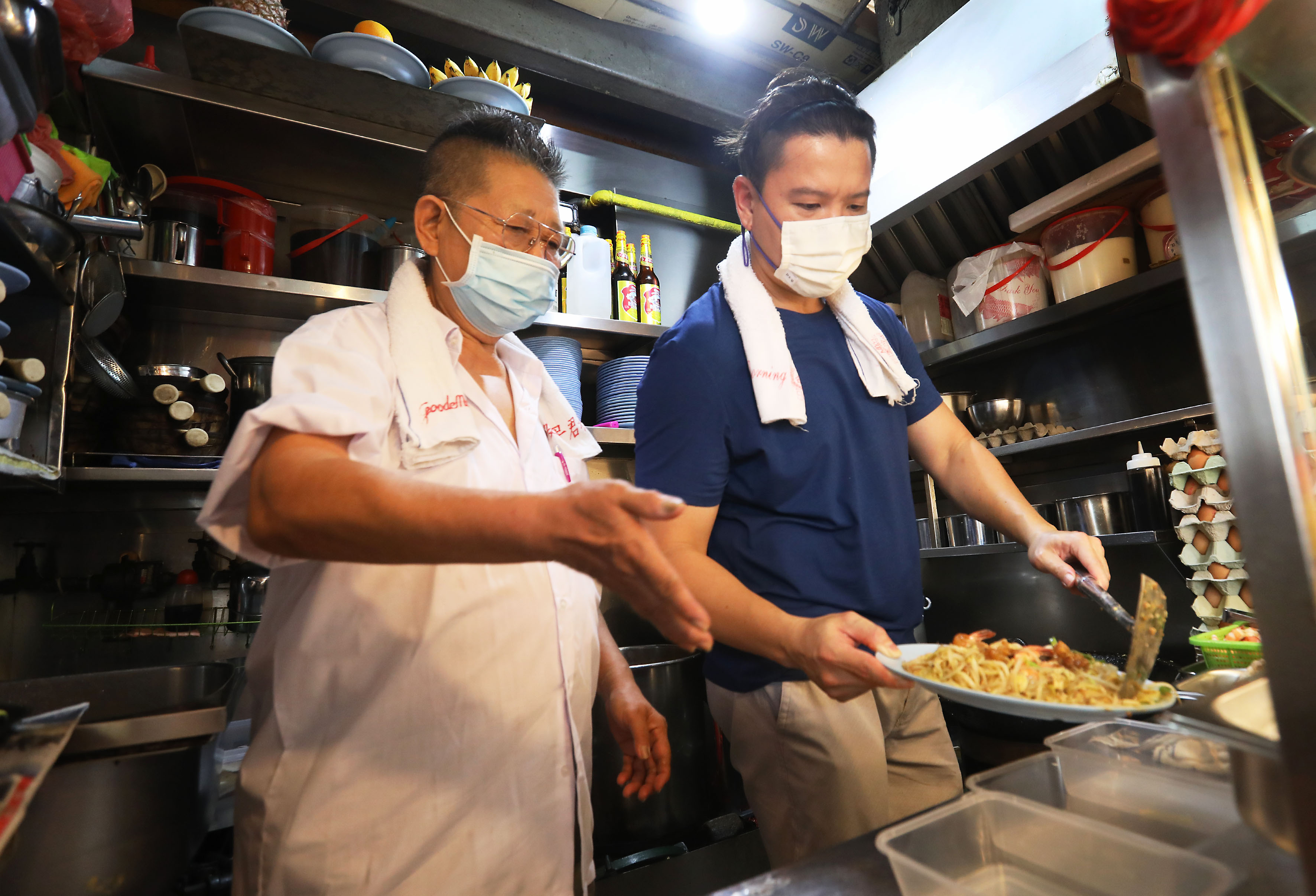 Mr Kiang Kaiming (L) showing his mentee Louis Wong how to serve Hokkien prawn noodles. u00e2u20acu2022 Photo by Raj Nadarajan for TODAY