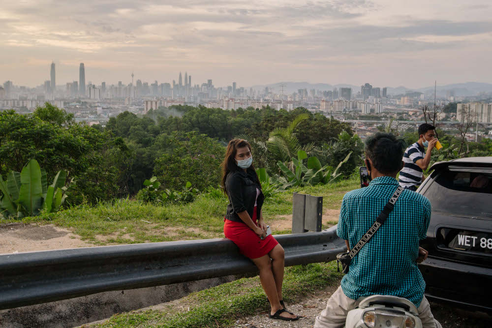 People wearing face masks pose for a picture on the roadside atop a hill with a view of the Kuala Lumpur skyline in Ampang January 31, 2020. u00e2u20acu201d Picture by Firdaus Latif