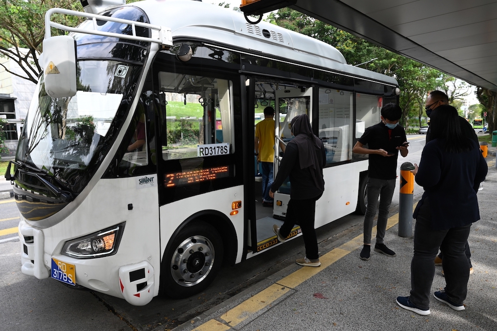 An employee (2nd right) checks the commuter application booking on a passenger's mobile phone before boarding an on-demand autonomous bus developed by ST Engineering at the start of a trial run from Singapore Science Park. u00e2u20acu201d AFP pic