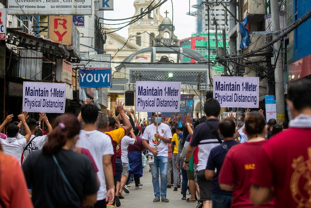A church worker carries a placard reminding mass-goers to maintain physical distancing to prevent the spread of the coronavirus disease, as Catholic devotees queue to attend mass on the feast day of the Black Nazarene, outside Quiapo Church in Manila, Phi