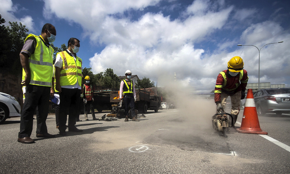 Johor exco Mohd Solihan Badri (2nd right) watches as a worker fills in a pothole in Johor Baru January 24, 2021. u00e2u20acu201d Bernama pic
