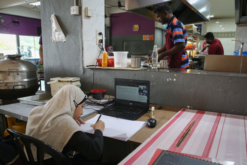 A Form One student takes part in an online class near her mother’s food stall in Shah Alam amid movement control order January 20, 2021. — Picture by Yusof Mat Isa