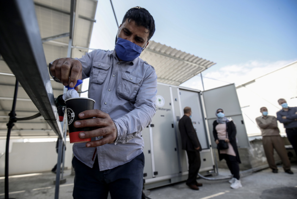 A Palestinian man fills a cup of water from a solar-powered water generator that extracts potable water straight from the air donated by Watergen. — AFP pic  