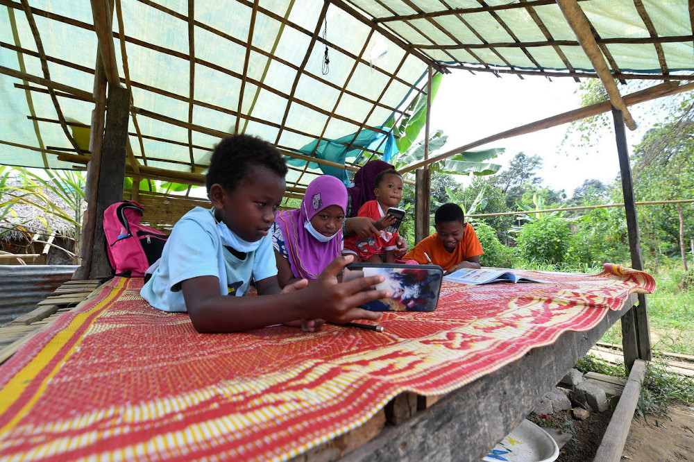 Orang Asli students Mohd Zakuan bin Zulkifli, and twins Norsuhayla Alya binti Zulkifli and Mohd Shadad bin Zulkifli take turns completing their homework using one handphone in Kampung Orang Asli Ulu Legong in Kedah, January 30, 2021. u00e2u20acu201d Bernama pic 