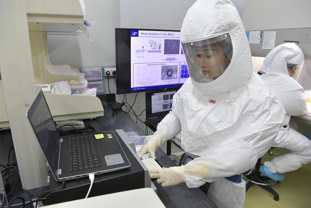 A scientist wearing personal protective equipment with powered air purifying respirator places samples into the polymerase chain reaction machine in the existing DSO biosafety lab. u00e2u20acu201d Ministry of Defence handout via TODAY