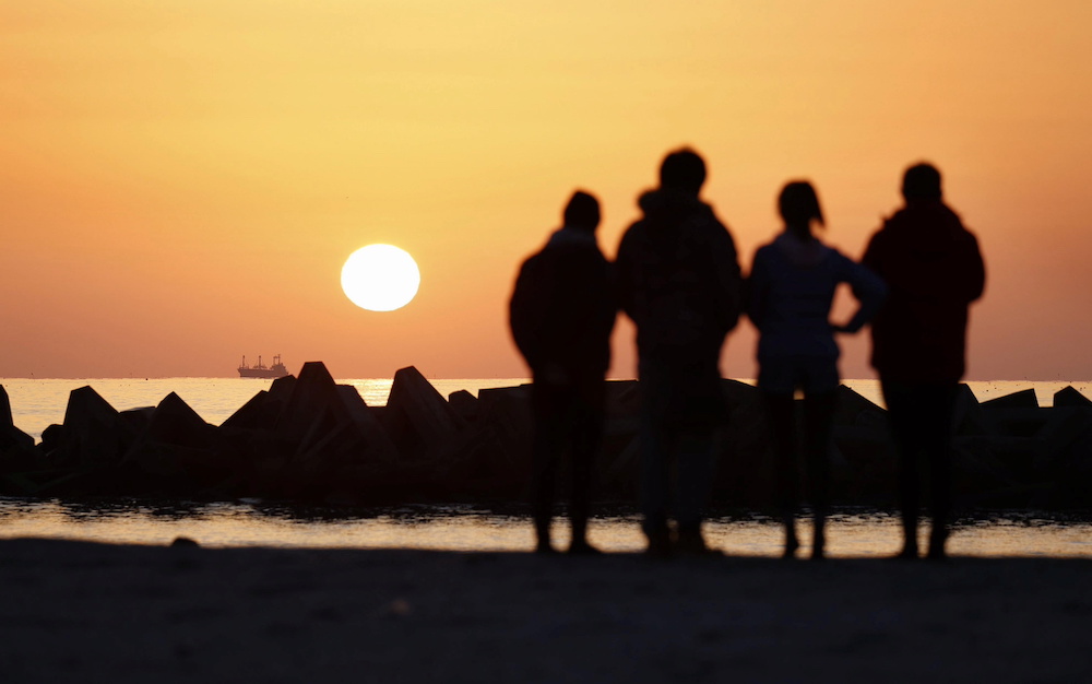 Local residents stand on the seashore at sunrise at Arahama district in Sendai, early March 11 2021, to mark the 10-year anniversary of the 2011 earthquake and tsunami that killed thousands and set off a nuclear crisis. u00e2u20acu201dKyodo handout via Reuters