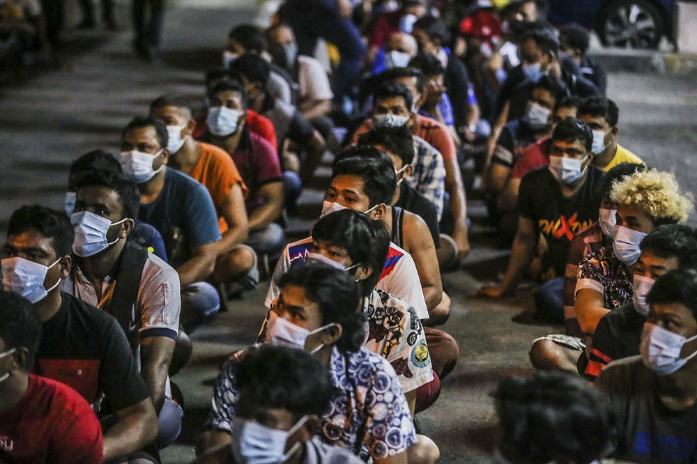Foreigners nabbed during a raid by the Kuala Lumpur Immigration Department are seen seated on the ground, outside the Ixora Apartment in Pudu March 6, 2021. u00e2u20acu201d Picture by Hari Anggara